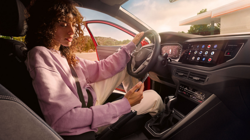 Une femme est au volant de la Taigo et regarde son téléphone portable. La voiture est garée et la porte conducteur est ouverte.