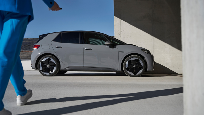 Une personne en costume bleu se rend vers une VW ID.3 grise en stationnement.