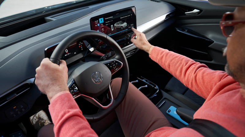 Ein Mann sitzt auf dem Fahrersitz eines VW Elektrofahrzeuges und bedient das Infotainmentsystem.