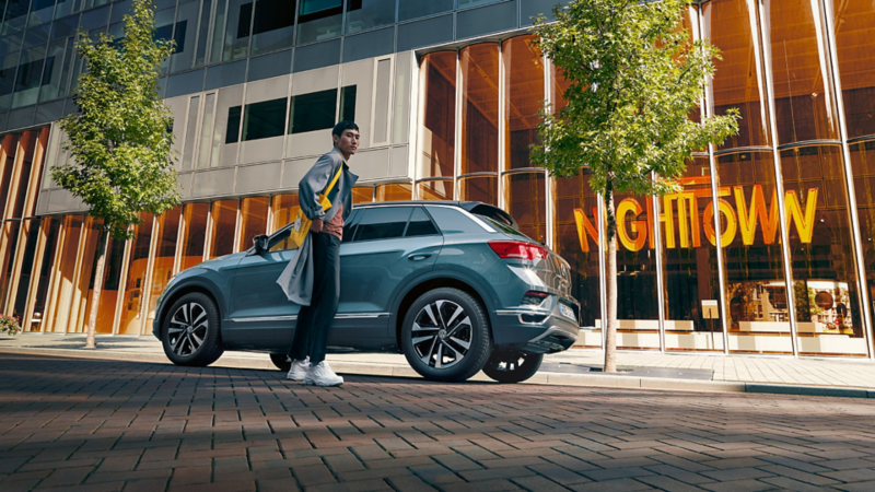 Volkswagen henkilöauto kuvattuna kadulla alaviistosta, auton edustalla seisoo henkilö