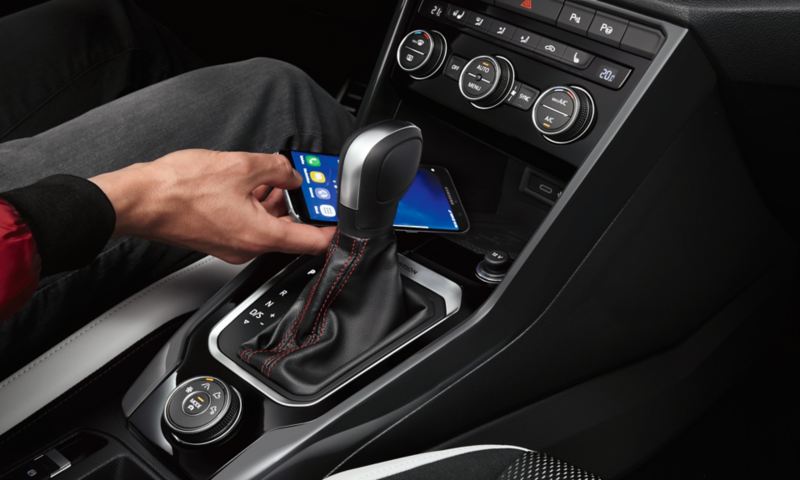 Wnętrze VW T-Roca ze złączem telefonicznym Comfort, mężczyzna kładzie smartfon na ładowarce indukcyjnej