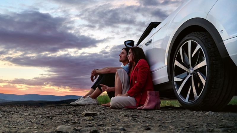 En man och en kvinna sitter på marken nedanför en Volkswagen