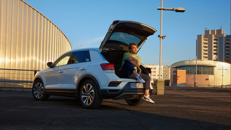 VW T-Roc ACTIVE blanche garée dans un environnement urbain avec un compartiment à bagages ouvert.
