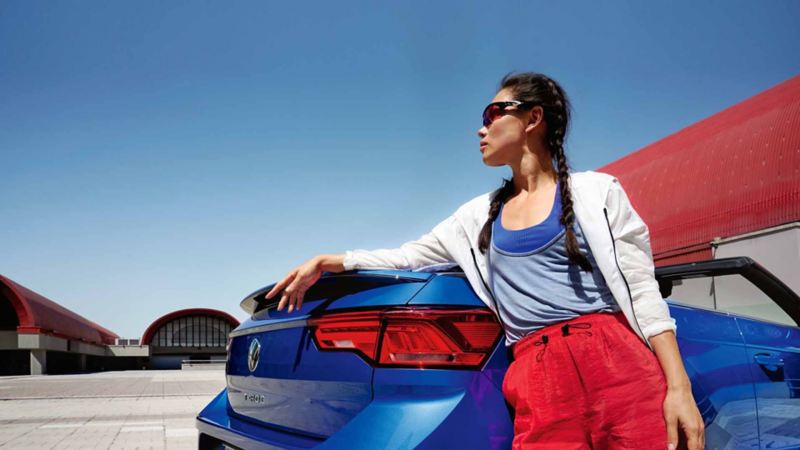 Una donna appoggiata alla sua cabriolet Volkswagen, vista posteriormente.