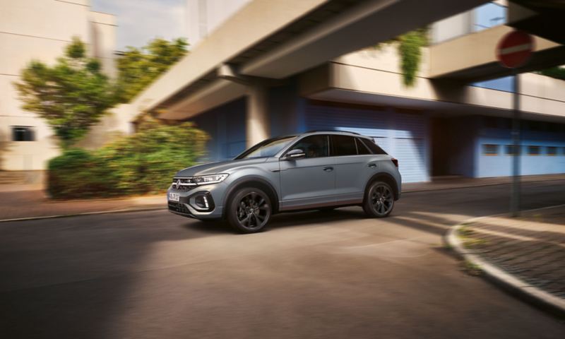 VW T-Roc R-Line in grey drives dynamically over intersection, visible from the side