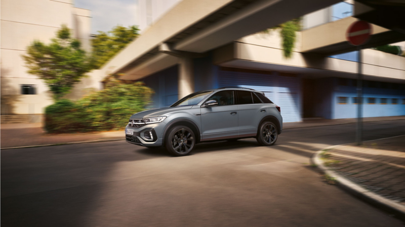 VW T-Roc R-Line in grey drives dynamically across intersection, view from the side.