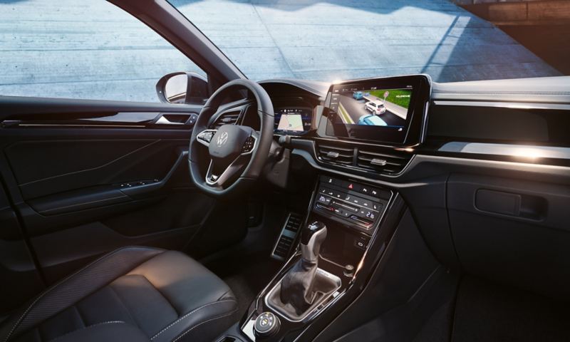 Intérieur de la VW T-Roc, vue depuis le siège du passager avant sur le siège du conducteur et le cockpit avec volant multifonction et système d’infodivertissement