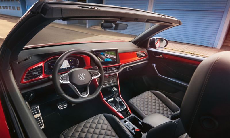 Intérieur du VW T-Roc Cabriolet : vue d'en haut à travers le toit ouvert sur le cockpit avec décor rouge et les sièges avant. 