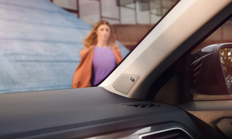 Vue détaillée du système sonore Beats Audio à l'intérieur du Volkswagen T-Roc. En arrière-plan, une femme avance vers le véhicule.