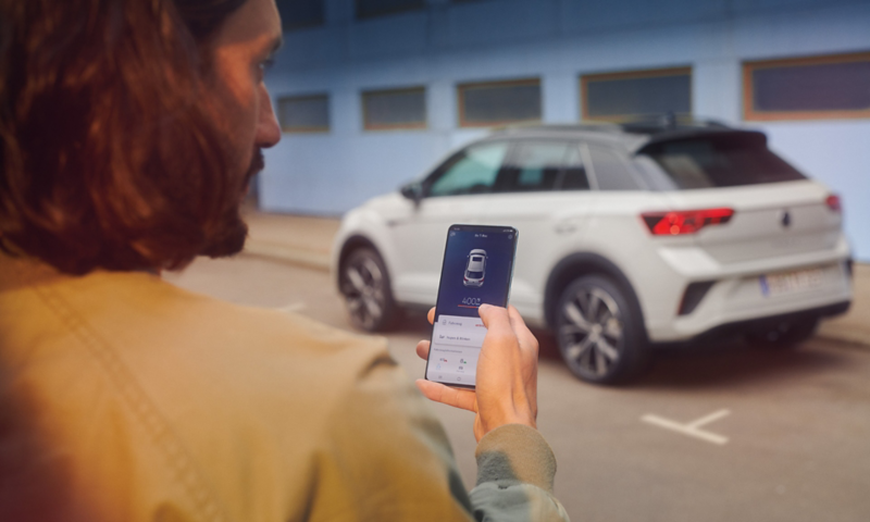 VW T-Roc R-Line en blanco delante de un edificio, lateral visible, hombre con smartphone en primer plano