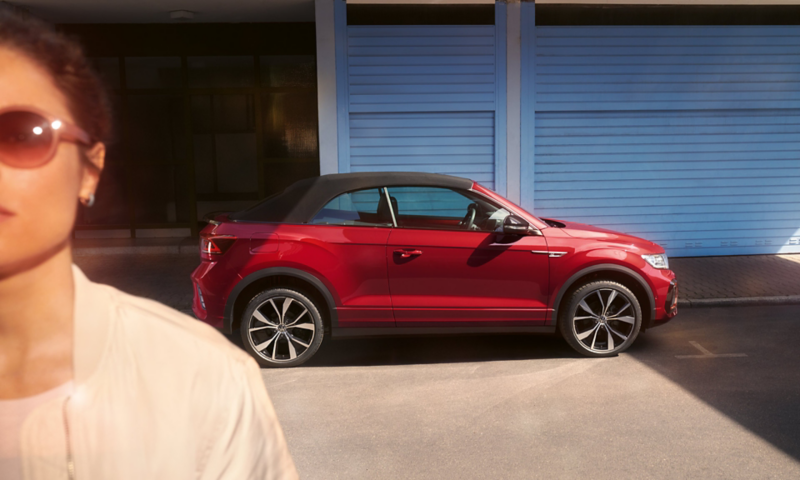 Un T-Roc Cabriolet rouge, capote en place, vu de profil avec la tête d'une femme au premier plan.