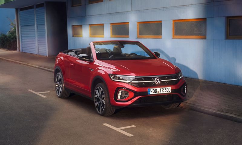 Front and side view of the red T-Roc Cabriolet with the roof open, parked on the side of the road.