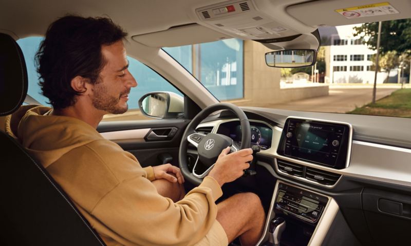 Blick in das Interieur des VW T-Roc MOVE,  ein junger Mann in beigem Hoodie nutzt die Sprachbedienung