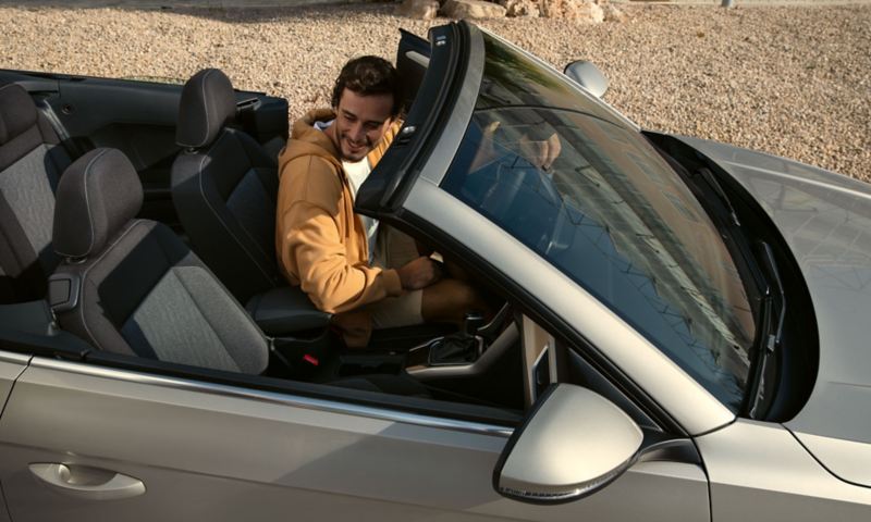 Blick in den Innenraum des VW T-Roc Cabriolet MOVE mit geöffnetem Dach, Ansicht von oben, am Steuer sitzt ein junger Mann