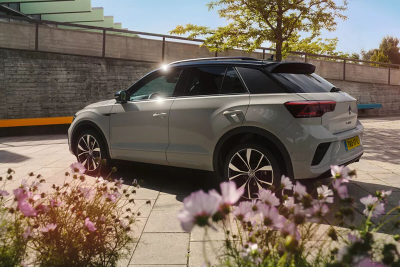Schuin achteraanzicht van de T-Roc R-Line in wit met zwart dak, er staan wat bloemetjes op de voorgrond