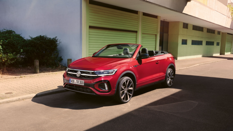 Ein rotes VW T-Roc Cabriolet mit geöffnetem Verdeck parkt am Straßenrand.