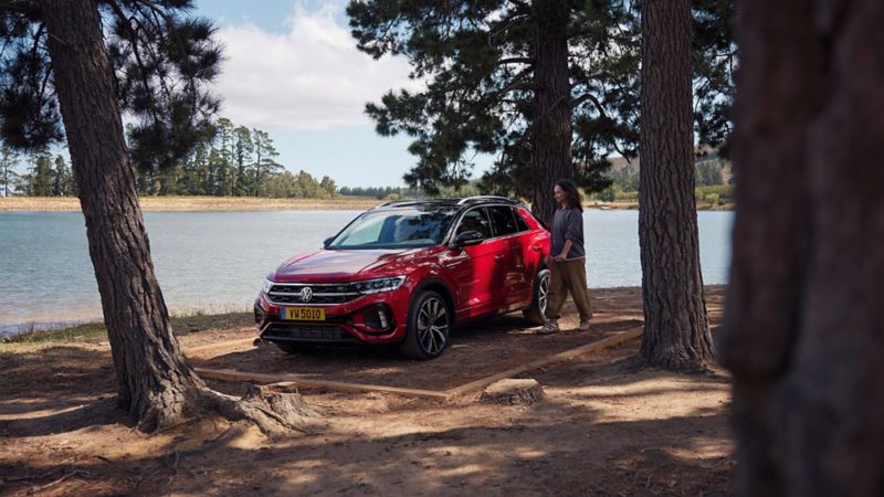 Un T-Roc rouge est garé au bord d'un lac et une femme s'approche de la voiture.