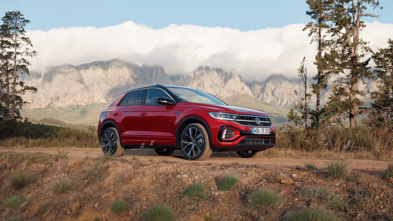 Red Volkswagen SUV parked on rugged terrain with mountains in the background.