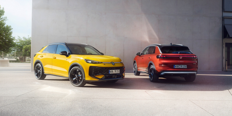 Ein gelber VW T-Roc und ein roter VW T-Roc stehen nebeneinander vor einem modernen Gebäude.