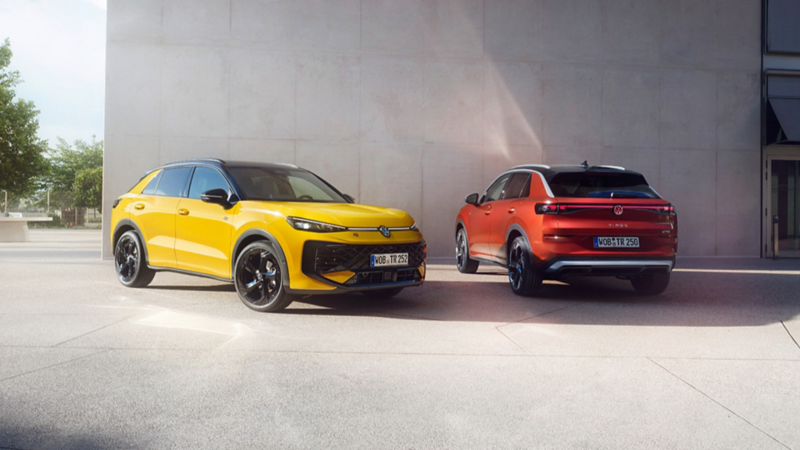 A yellow VW T-Roc R-Line and a red VW T-Roc Style standing next to each other in front of a modern building.