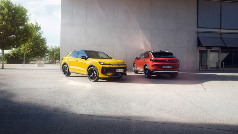 Un VW T-Roc R-Line jaune et un VW T-Roc Style rouge côte à côte devant un bâtiment moderne.