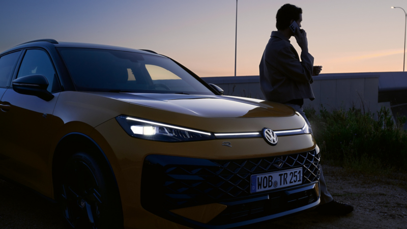 Un homme aux côtés d’un VW T-Roc R-Line avec les phares allumés et le logo illuminé.