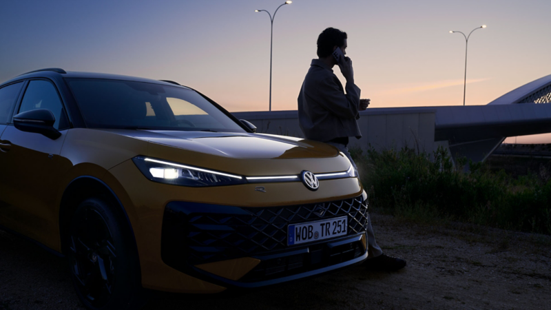 Ein Mann neben einem VW T-Roc R-Line mit eingeschalteten Scheinwerfern und beleuchtetem Logo.
