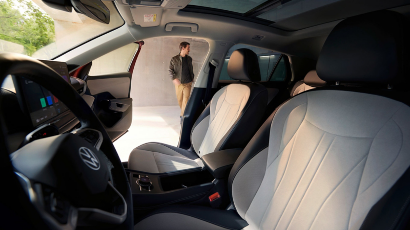 Vue intérieure d'un T-Roc photographiée depuis le siège conducteur. La porte passager est ouverte et on aperçoit un homme à l'extérieur de la voiture.