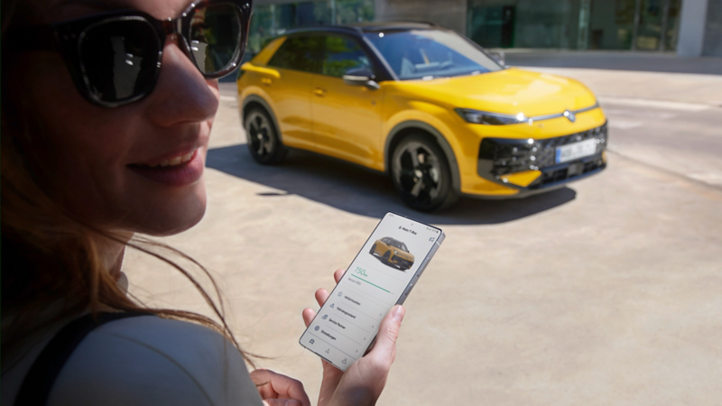 A woman uses the VW Connect app next to her VW T-Roc R-Line.