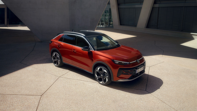 A red VW T-Roc Style stands in front of a modern building in sunlight.