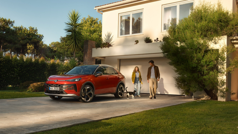 EN röd T-Roc står parkerad utanför ett hus. En man och en flick går bakom bilen