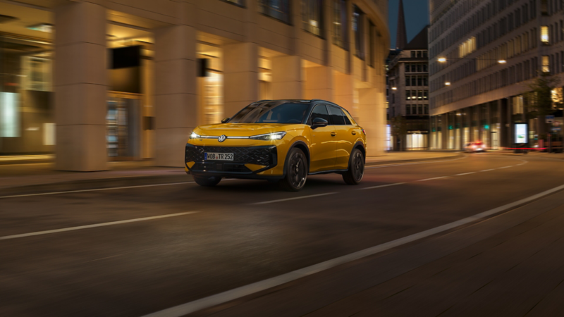 Un VW T-Roc R-Line jaune circule dans un environnement urbain la nuit.