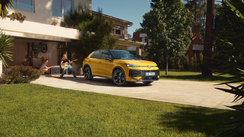 En ny VW T-Roc R-Line står parkerad utanför ett garage, en tjej spelar gitarr medan en man sköter ljudet