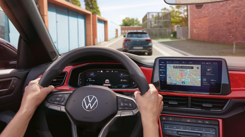Eine Person fährt ein VW T-Roc Cabriolet mit aktiver Navigation auf dem Display des Infotainment-Systems.