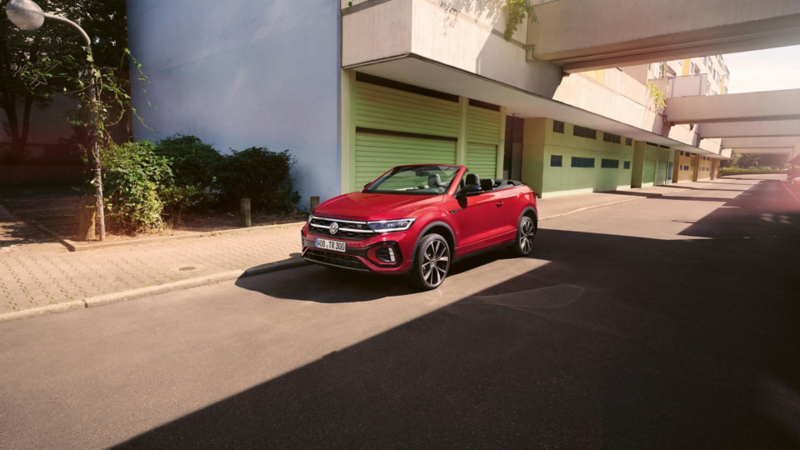 Ein rotes VW T-Roc Cabriolet mit geöffnetem Verdeck parkt am Straßenrand.
