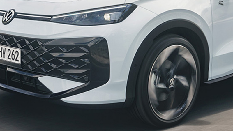 Biały VW T-Roc hybrid jedzie wiejską drogą z lasem w tle.