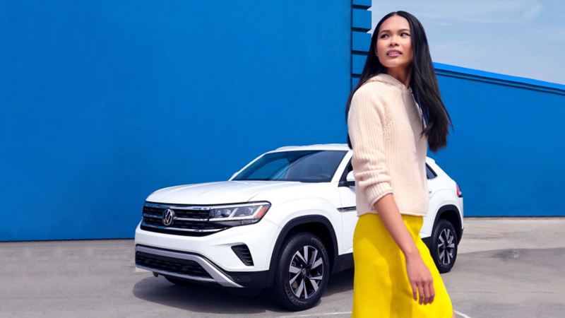 A woman staying next to the Pearl White Volkswagen Atlas