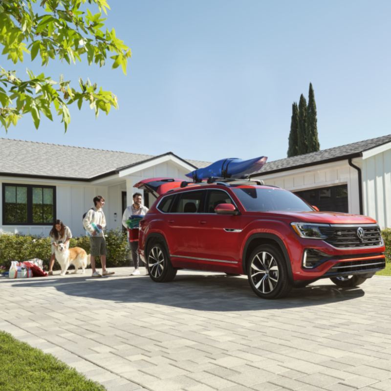 A family of three and a dog loading up the trunk of a red VW Atlas getting ready to go on a trip.