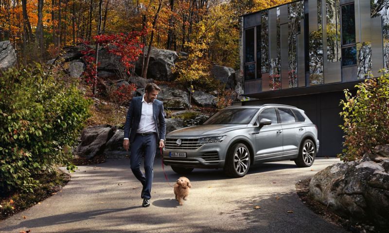 A man and his dog are walking in front of a VW Touareg