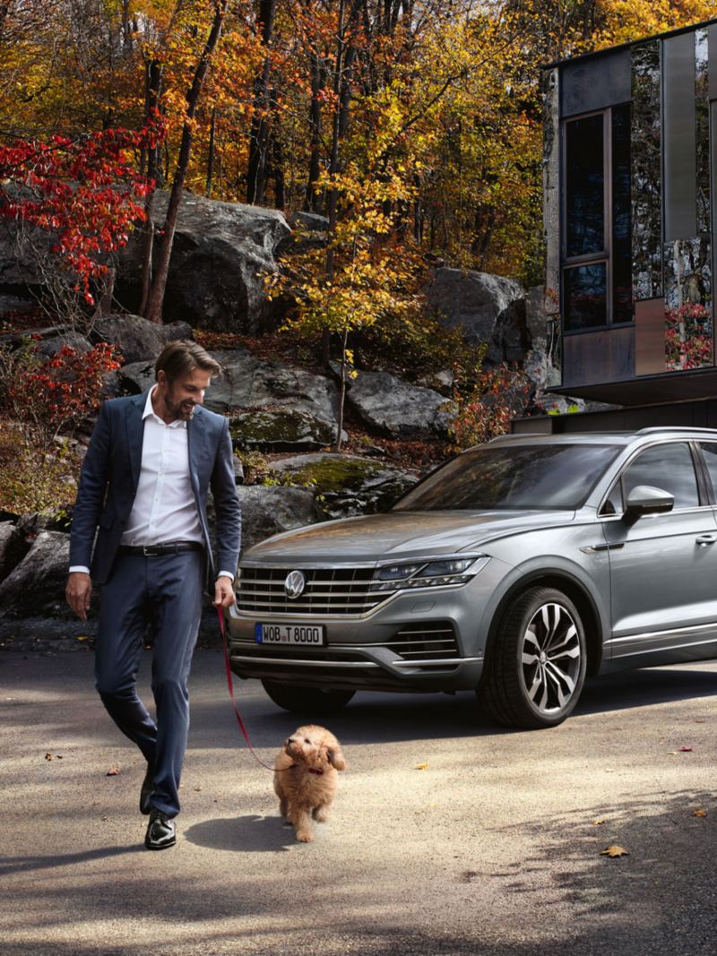 A man and his dog are walking in front of a VW Touareg