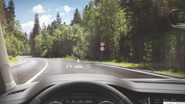 A man sitting in the front seat of a parked VW Touareg R-Line looks smilingly into the camera.