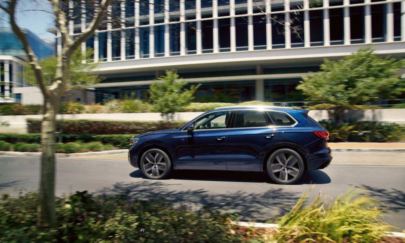 A VW Touareg R-Line drives across a road, view from the side.