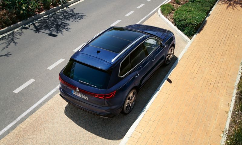 Een VW Touareg R-Line staat geparkeerd aan de kant van de weg, schuin bovenaanzicht vanaf de achterkant en het glazen panoramadak.