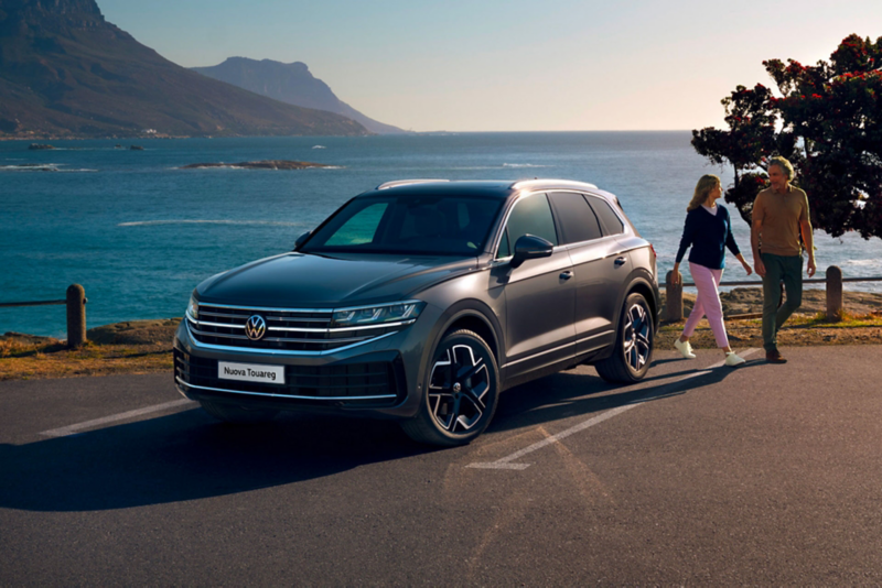 Una VW Touareg Elegance è parcheggiata al sole, vista frontalmente di sbieco, dietro si vedono il mare e la costa.