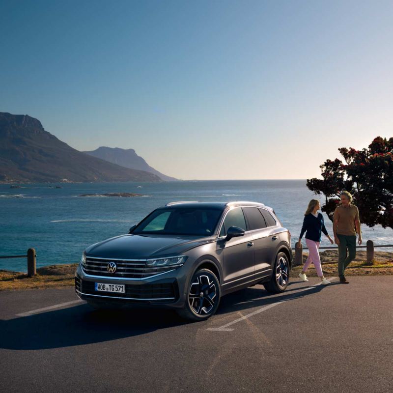 VW Touareg Elegance parkerad i solen, sedd snett framifrån. Bakom bilen syns havet.