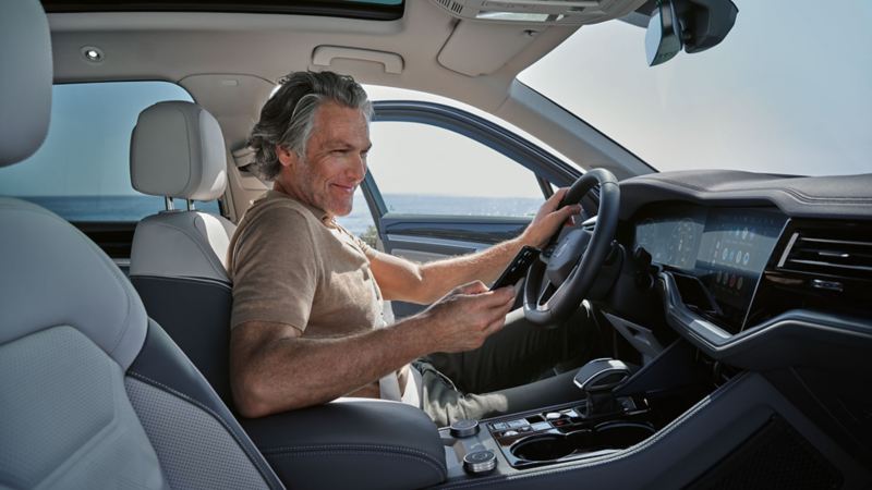 Ein Mann in einem parkenden VW Touareg Elegance verbindet sein Smartphone per Wireless App Connect mit dem VW Touareg Elegance.