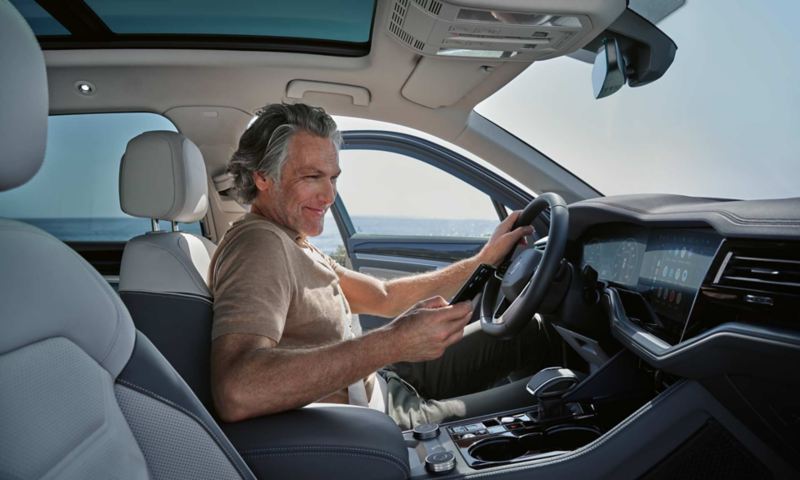 Un homme dans une VW Touareg Elegance en stationnement connecte son smartphone à la VW Touareg Elegance sans fil via App-Connect.