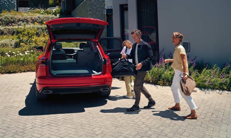 Un homme et une femme marchent en direction d'un VW Touareg Elegance eHybrid avec le coffre ouvert.