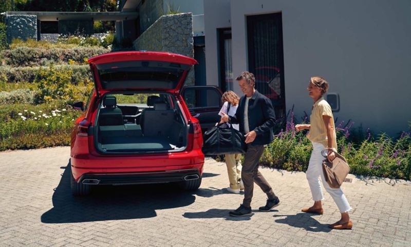 Mężczyzna i kobieta zbliżają się do VW Touarega Elegance eHybrid z otwartym bagażnikiem.