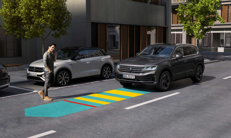 A man crosses a road, the Front Assist of the approaching VW Tiguan recognizes him and warns the driver.